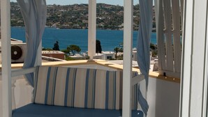 Una cama con dosel blanco con cojines a rayas azules y blancas, vista al mar y suelo de baldosas.