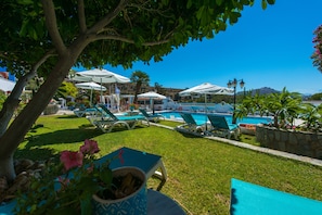 A pool area with lounge chairs and umbrellas, surrounded by greenery and a clear sky. - Saraya Resort (Leros)