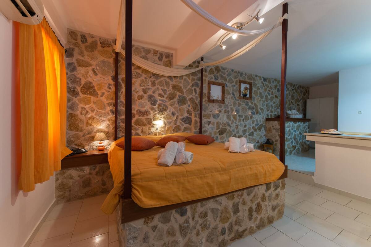 Un dormitorio con pared de piedra, cama con dosel, mesita de noche y mesilla con lámpara.