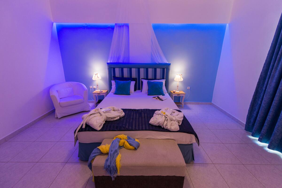 Un dormitorio con cama, mesitas de noche, una silla y un banco.