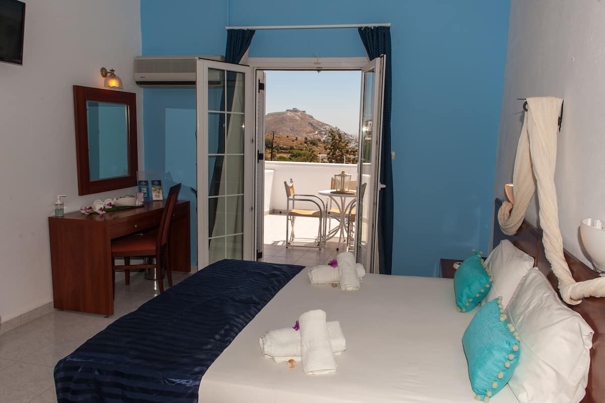 Habitación de hotel con cama, escritorio, silla y vista a la montaña desde una puerta abierta.