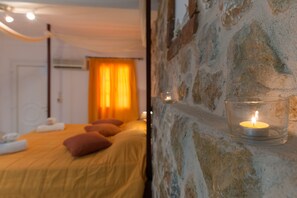 A bedroom with a stone wall, a bed with yellow bedding, and a lit candle in a glass holder.