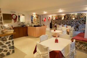 A dining area with stone walls, white chairs, and tables set for a meal.