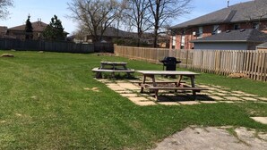 A backyard with a grassy lawn, two picnic tables, a barbecue grill, and a wooden fence. - Glenhaven Motel (Saint Thomas)