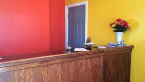 A reception desk with a wooden finish, a bear figurine, a vase with flowers, and a door in the background. - Glenhaven Motel (Saint Thomas)