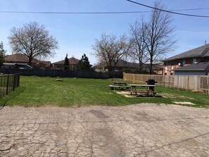 A backyard with a lawn, picnic tables, and a barbecue grill.