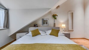 A bedroom with a bed, a bedside table, a lamp, a picture frame, and a window with curtains.