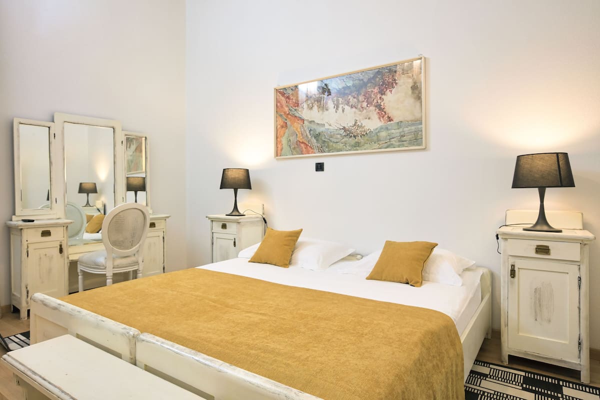 Une chambre à coucher bien rangée, avec un lit, des tables de chevet, un miroir et un tableau accroché au mur.