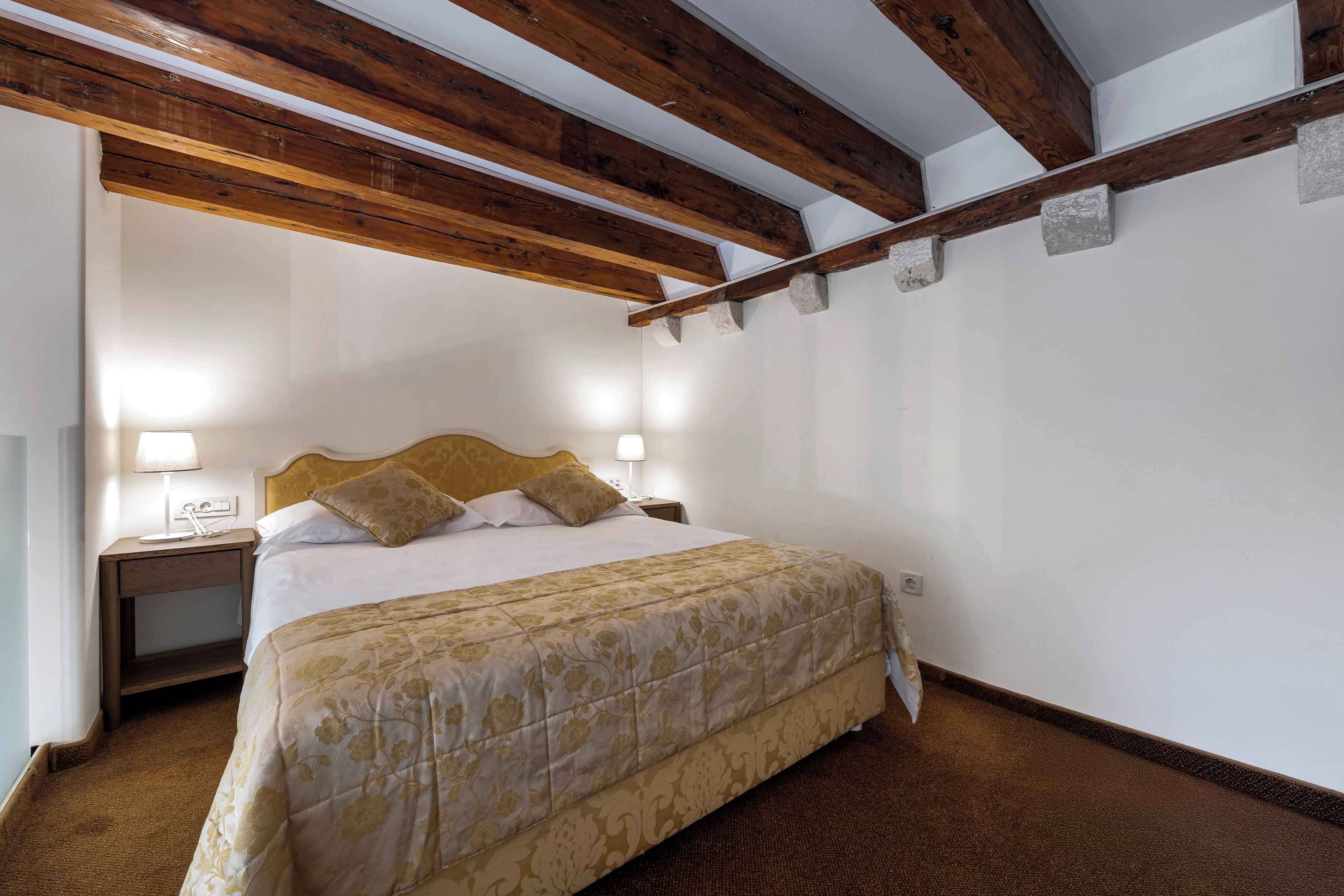 Un dormitorio con cama, lámparas de noche, techo de madera y suelo alfombrado.