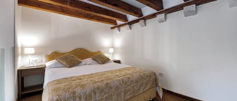 A bedroom with a bed, bedside lamps, a wooden ceiling, and a carpeted floor.