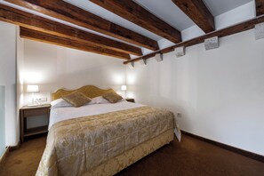 A bedroom with a bed, bedside lamps, a wooden ceiling, and a carpeted floor.