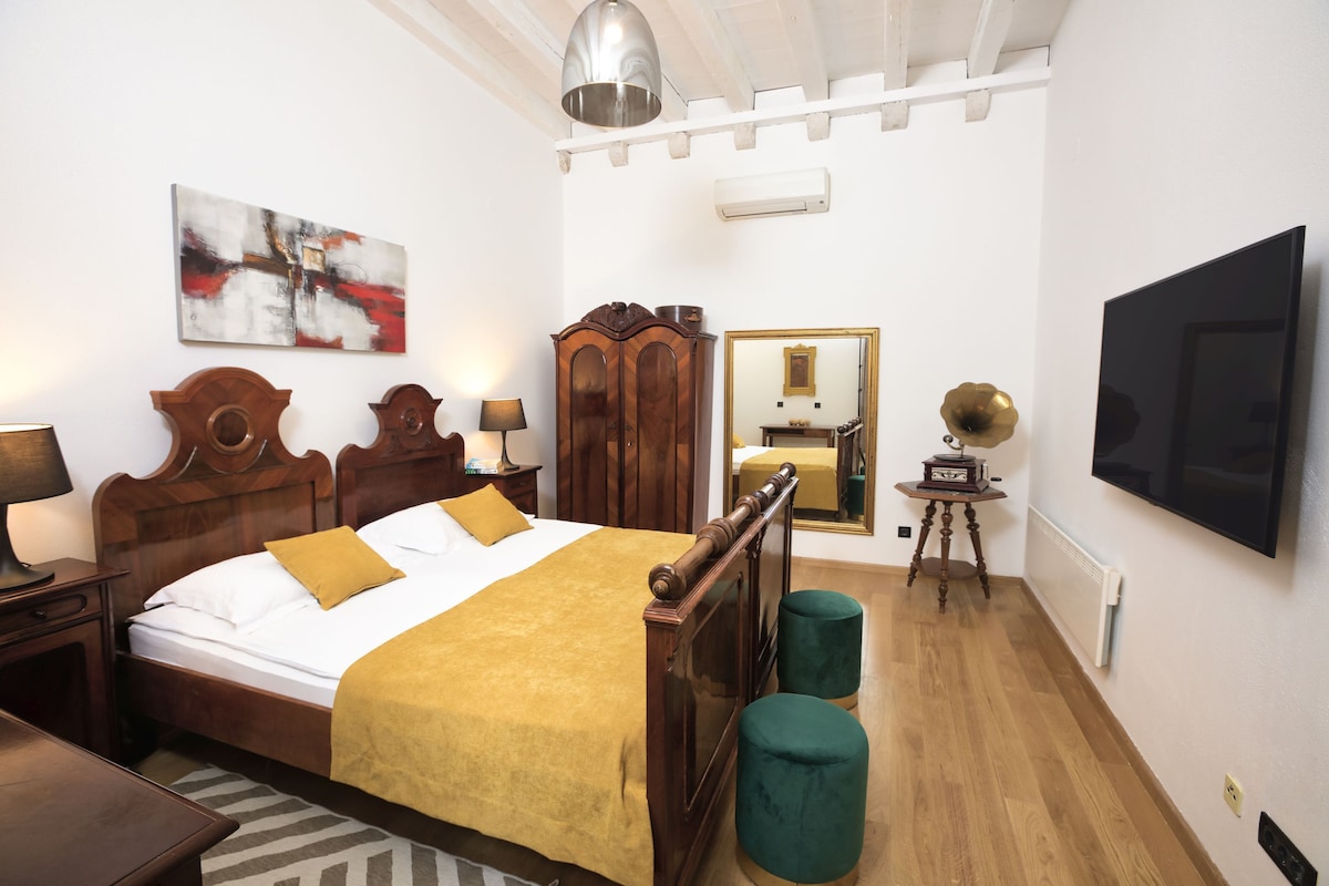 A bedroom with a wooden bed, a large mirror, a television, and a ceiling light fixture.