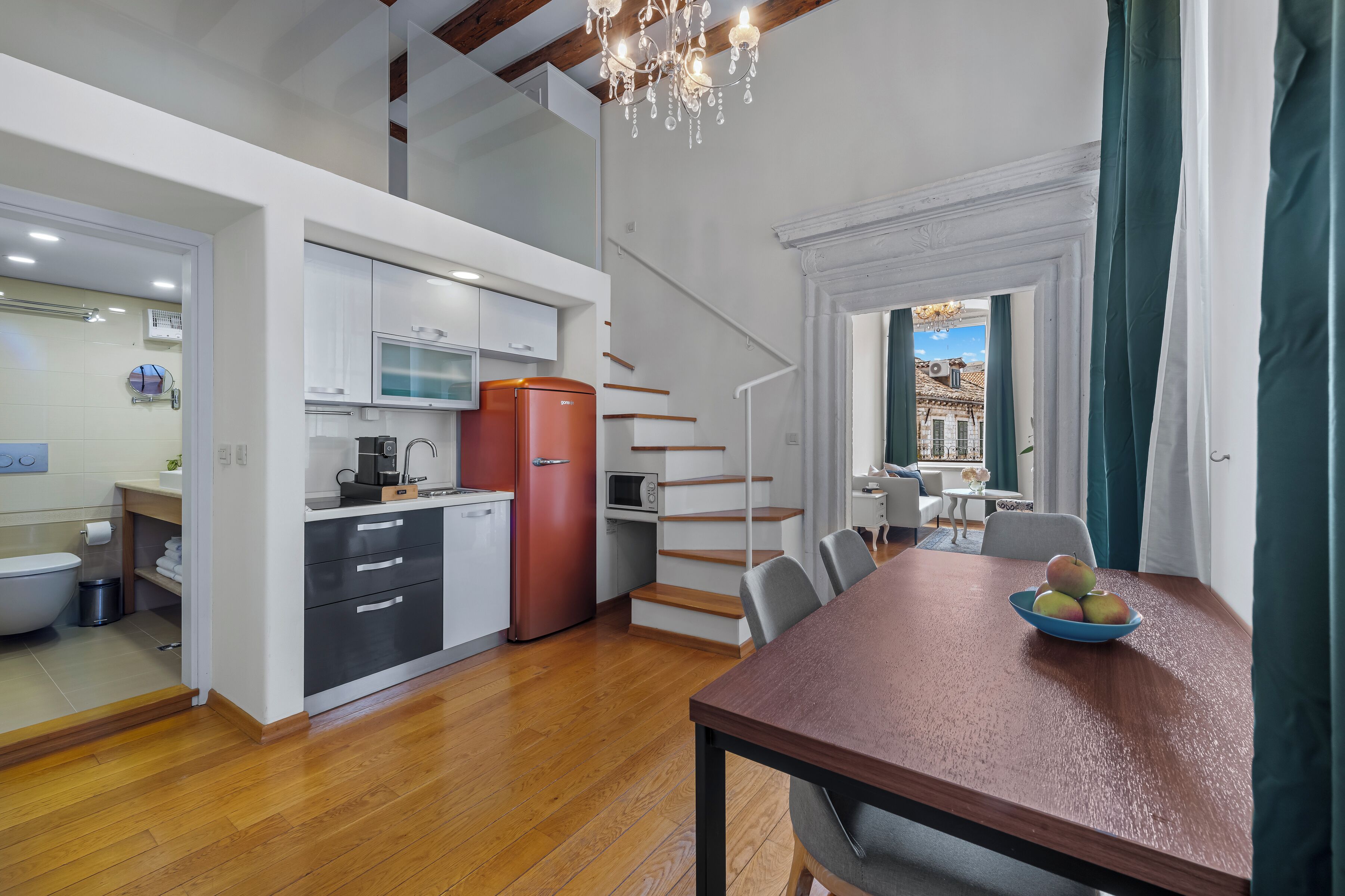 Una cocina moderna con un refrigerador rojo, piso de madera y un comedor con mesa y sillas.