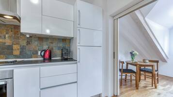 A modern kitchen with white cabinets, a stone backsplash, and a dining area with a wooden table and chairs.