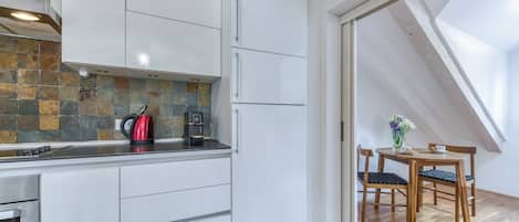 A modern kitchen with white cabinets, a stone backsplash, and a dining area with a wooden table and chairs.