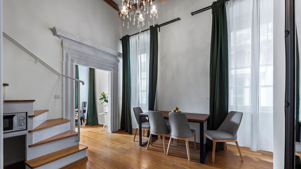 A modern living room with a wooden staircase, a dining area with four chairs, and a chandelier.