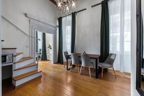 Un salon moderne avec un escalier en bois, un coin repas avec quatre chaises et un lustre.