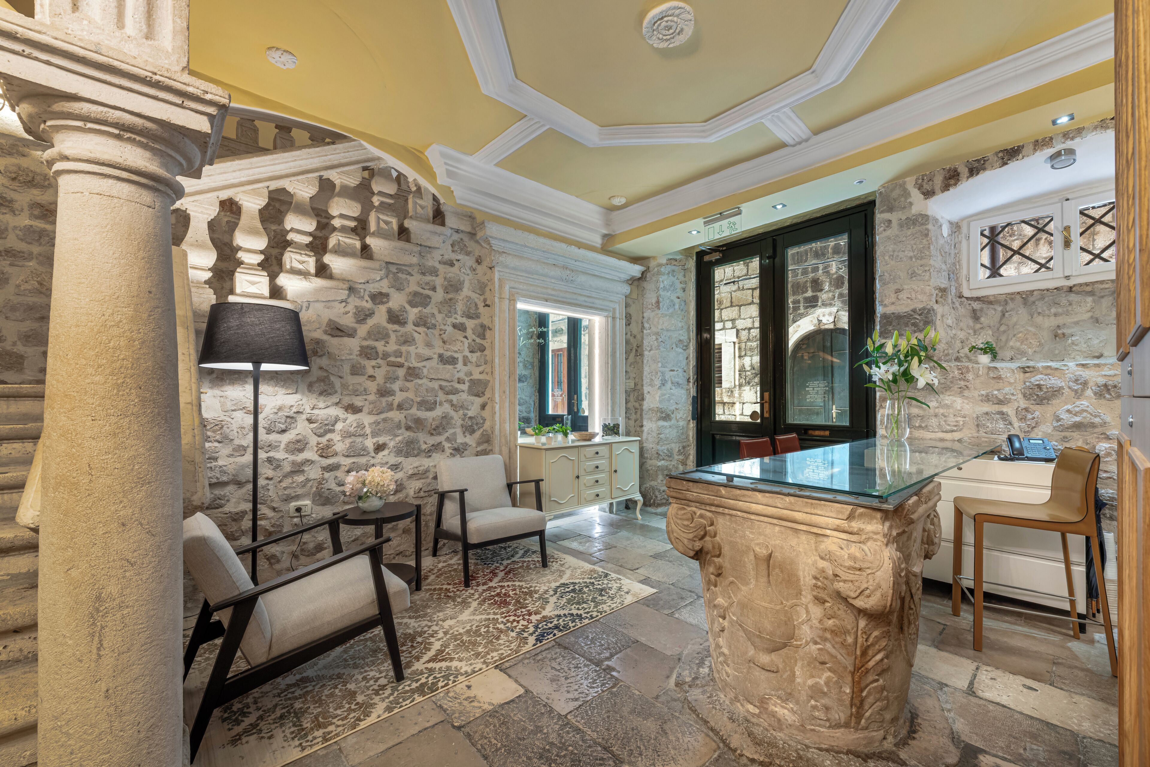 A room with stone walls, a glass-top table, a lamp, and a chair.