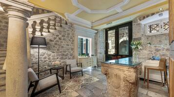 A room with stone walls, a glass-top table, a lamp, and a chair.