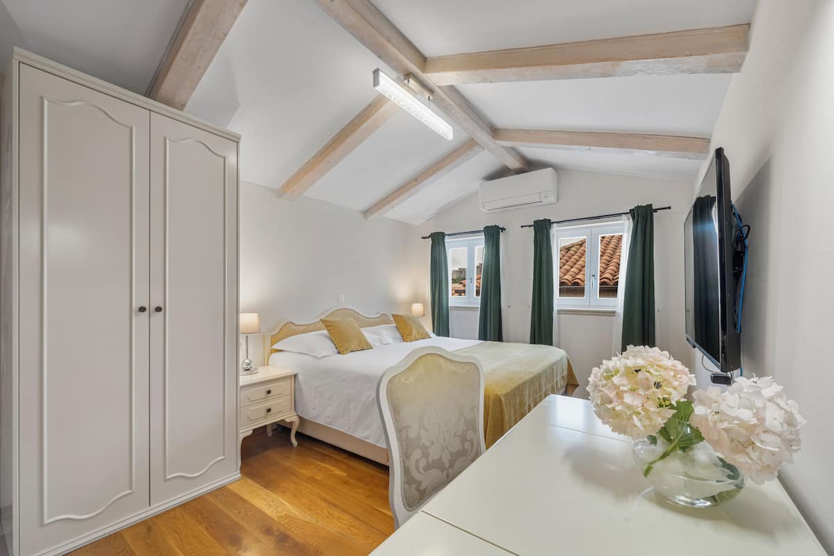 Une chambre à coucher comprenant un lit, une table de chevet et une commode. Il y a une fenêtre avec des rideaux et un téléviseur à écran plat fixé au mur.