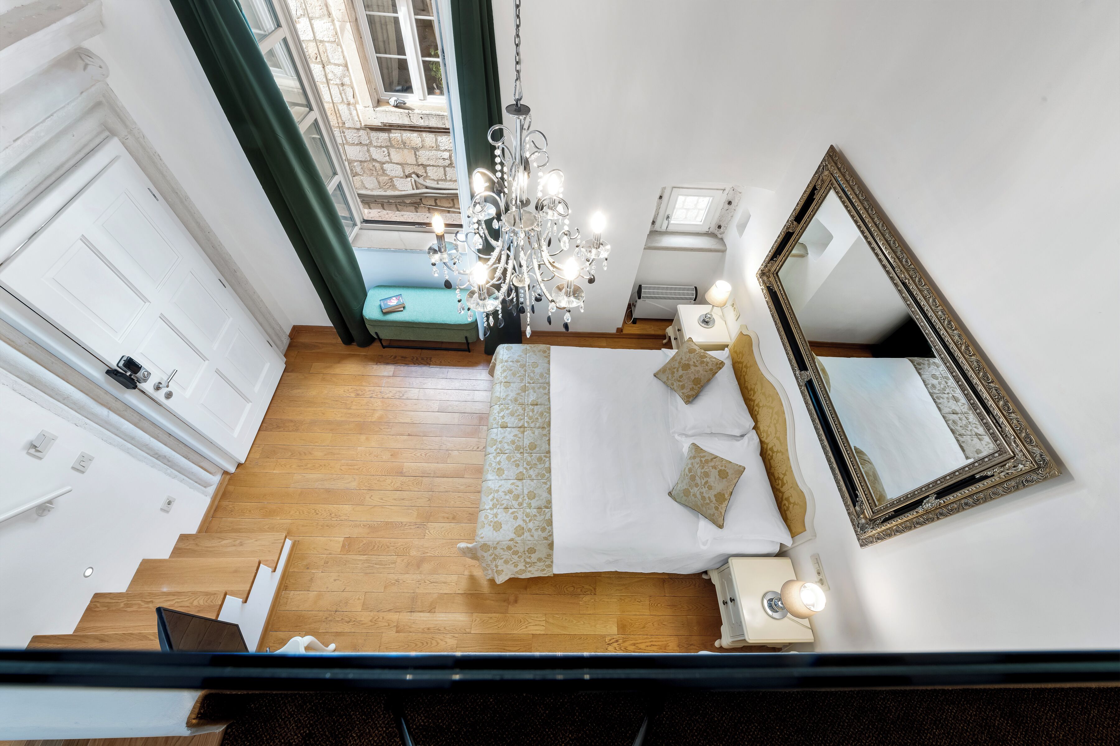 A bedroom with a bed, a chandelier, a mirror, and a view of the outside.