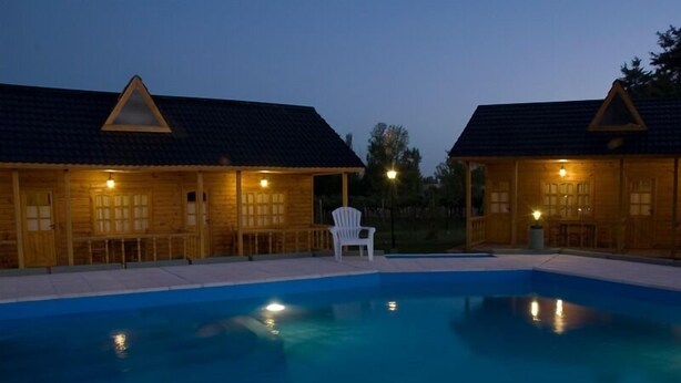 A swimming pool area with two wooden cabins, each with a triangular roof and a single window. - Vistalba Lodge (Luján de Cuyo)