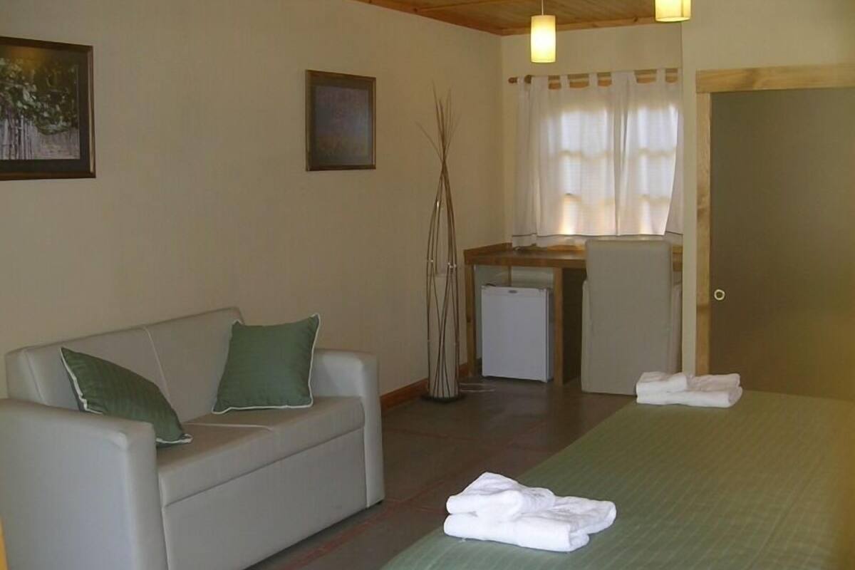 A room with a bed, a sofa with green cushions, a small kitchenette, and a door.