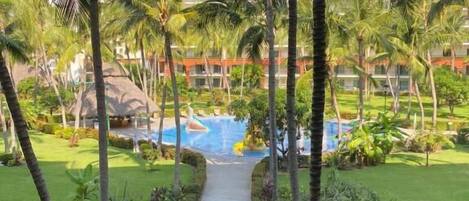 Un resort con piscina, palmeras y un camino que lleva a la piscina.