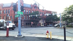 A street intersection with a fire hydrant, traffic lights, and a building with a red brick facade. - Imperial Motel (Cortland)