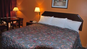 A hotel room with a bed, two bedside lamps, a desk with a chair, and a painting on the wall. - Imperial Motel (Cortland)