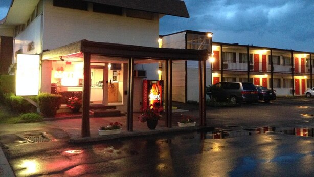 A motel with a covered entrance, a parking lot, and a building with multiple windows and doors. - Imperial Motel (Cortland)