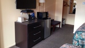 A hotel room with a flat-screen TV, a small desk with a lamp, a microwave, a chair, and a bed with a floral bedspread. - Imperial Motel (Cortland)