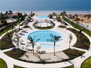 A resort with a central circular pool, lounge areas with sunbeds, and a view of the ocean. - Unlimited Luxury Villas - Del Canto Condo (Nuevo Nayarit)