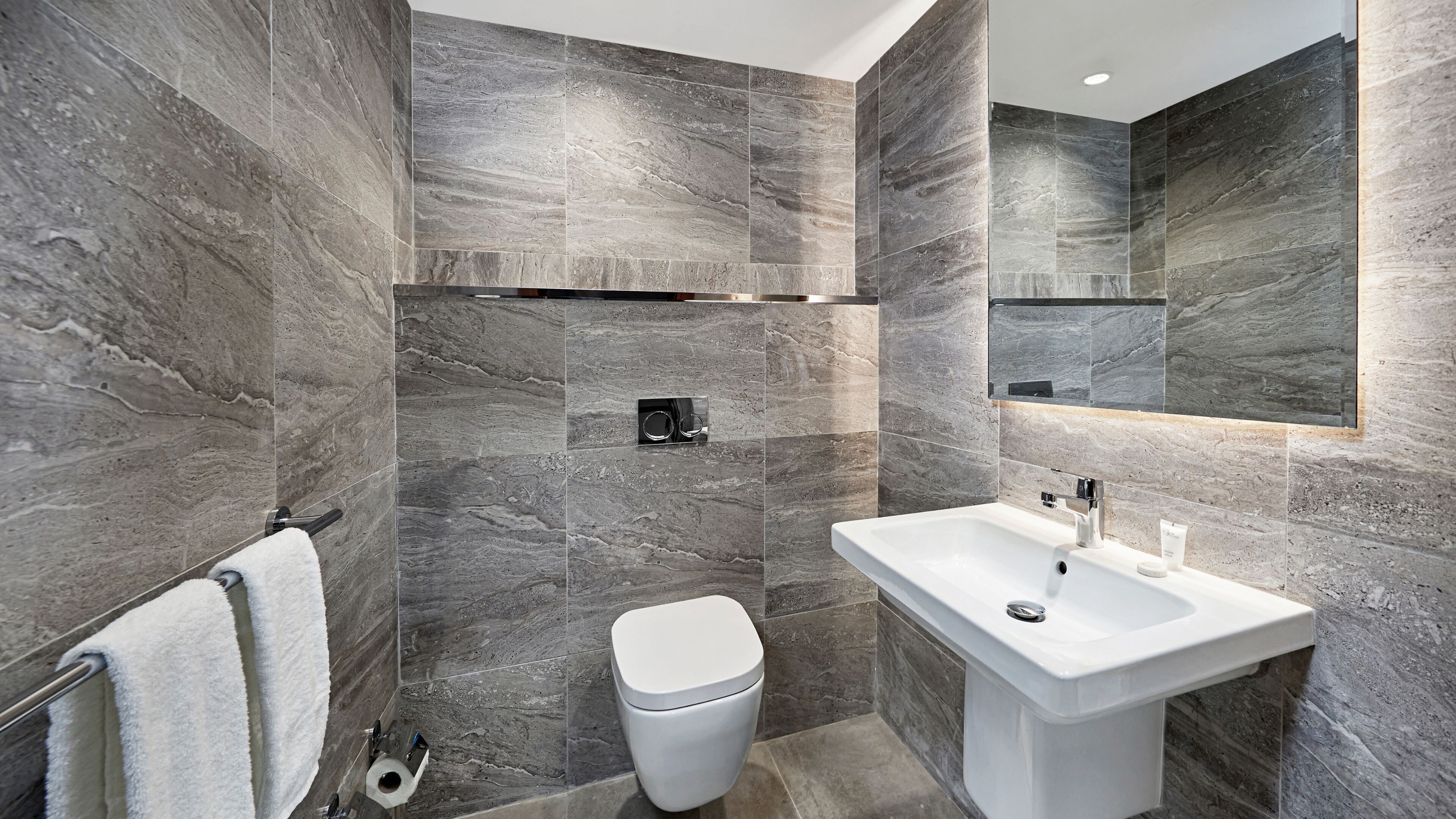 A modern bathroom with a large mirror, a white sink, and a toilet.