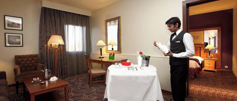 A hotel room with a dining table set, a sofa, a chair, a lamp, and a mirror.