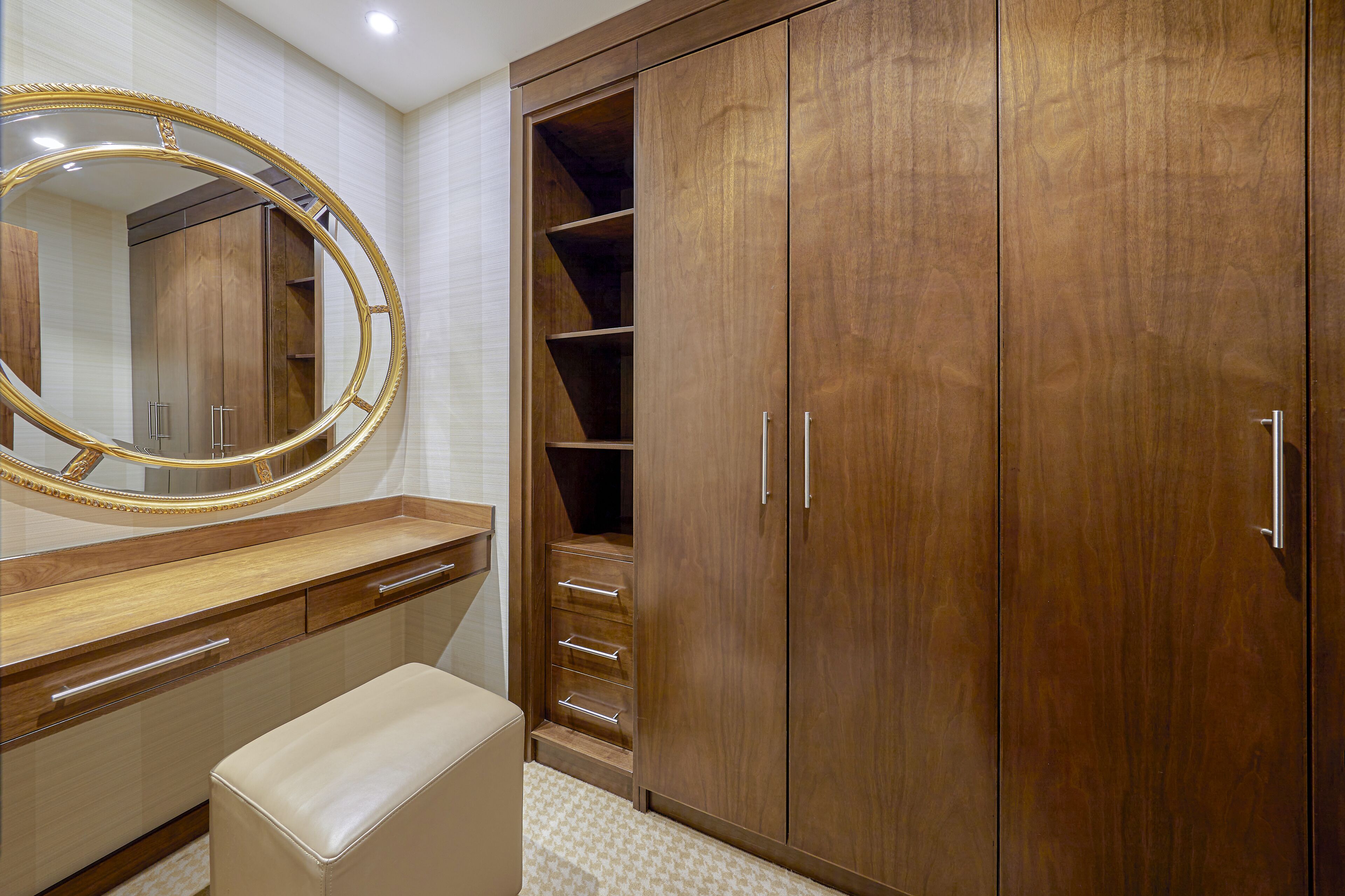 A bathroom with a wooden vanity, a large mirror, and a walk-in closet with drawers and shelves.