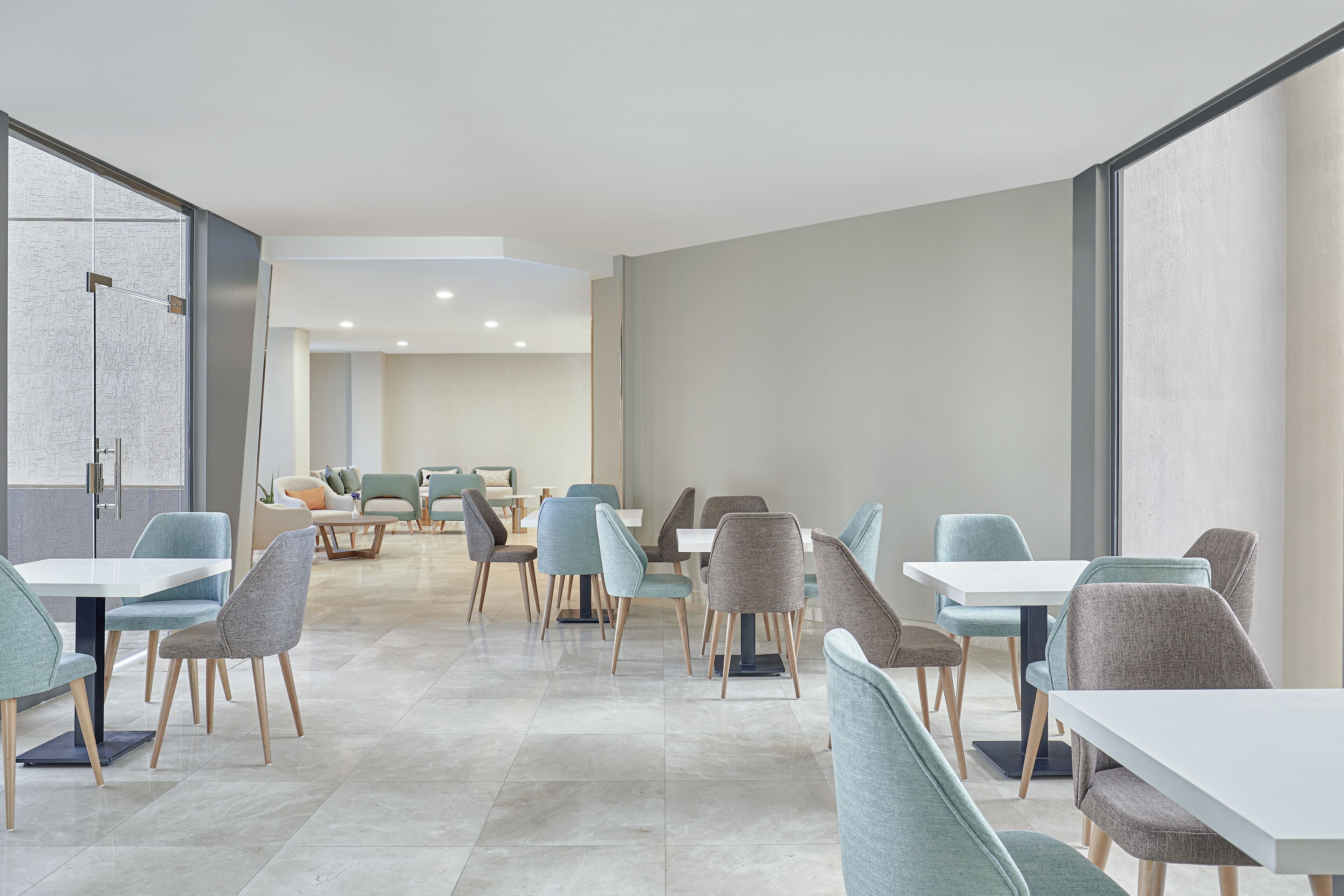 Ein moderner Essbereich mit mehreren Tischen und Stühlen, großen Fenstern und einem klaren, minimalistischen Design.