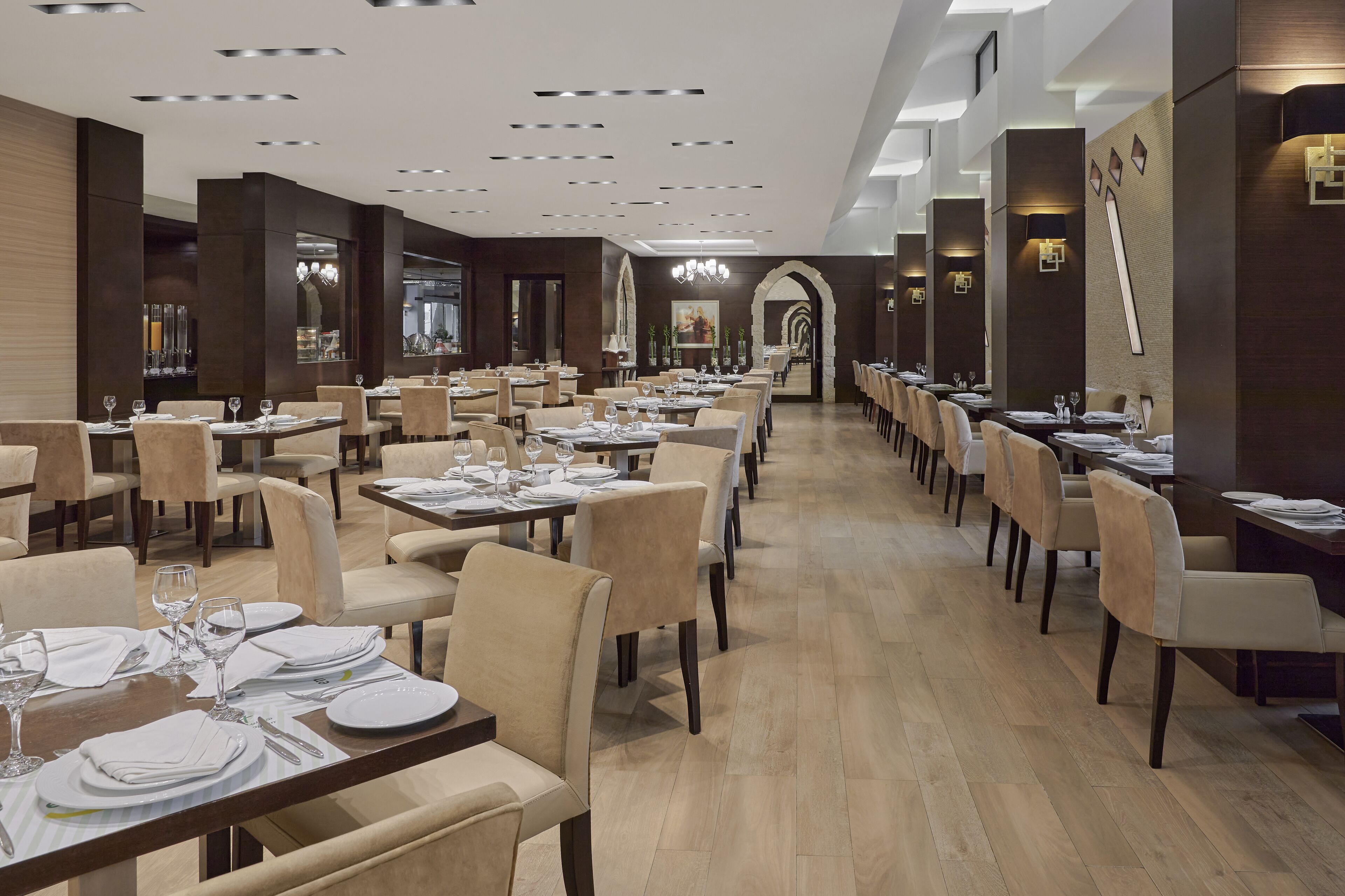 A spacious restaurant with multiple dining tables and chairs, modern lighting fixtures, and a clean, contemporary design.