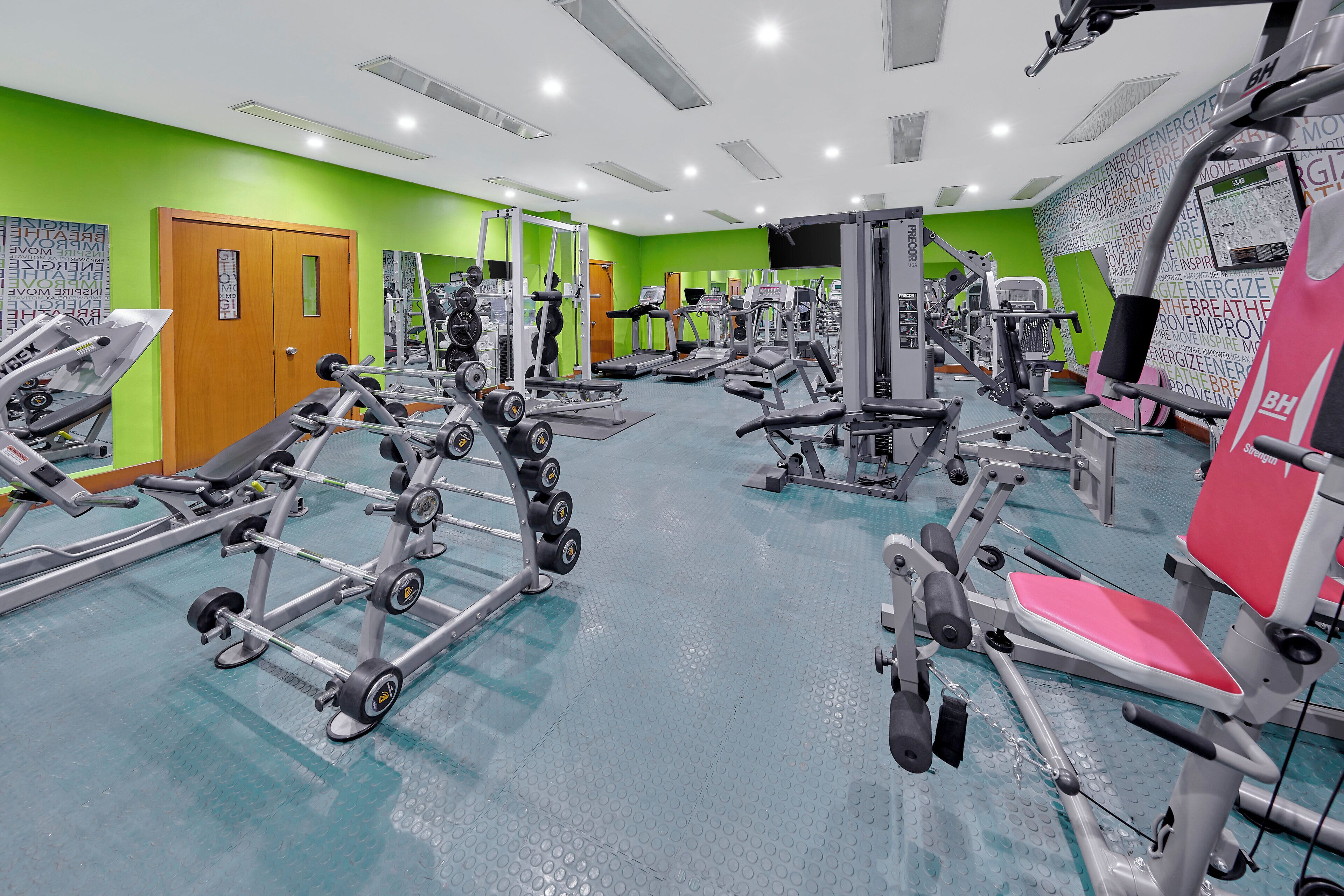 A gym with various exercise machines, a green wall, and a door.