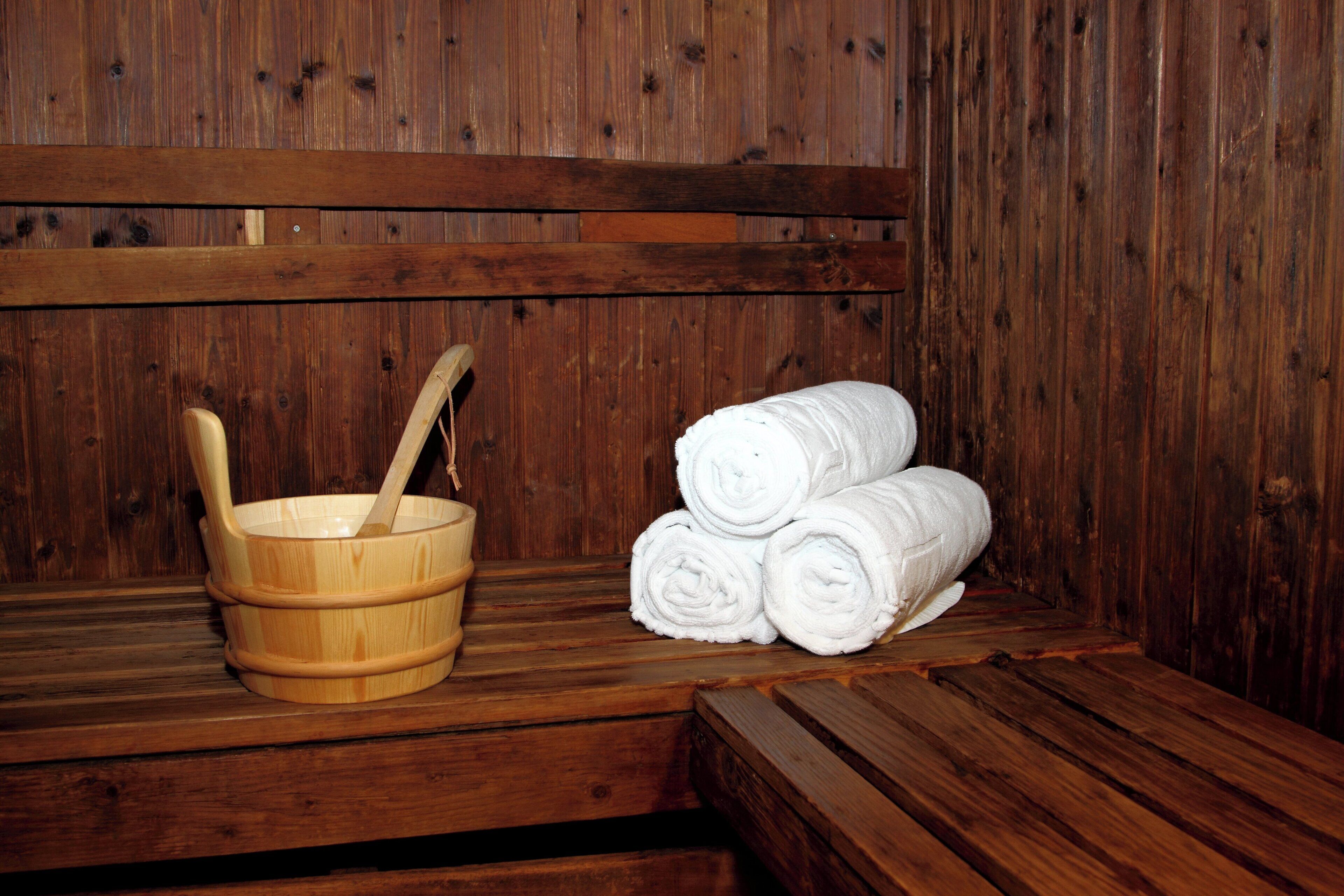 A wooden sauna with a wooden tub, a wooden bucket with a ladle, and rolled towels.