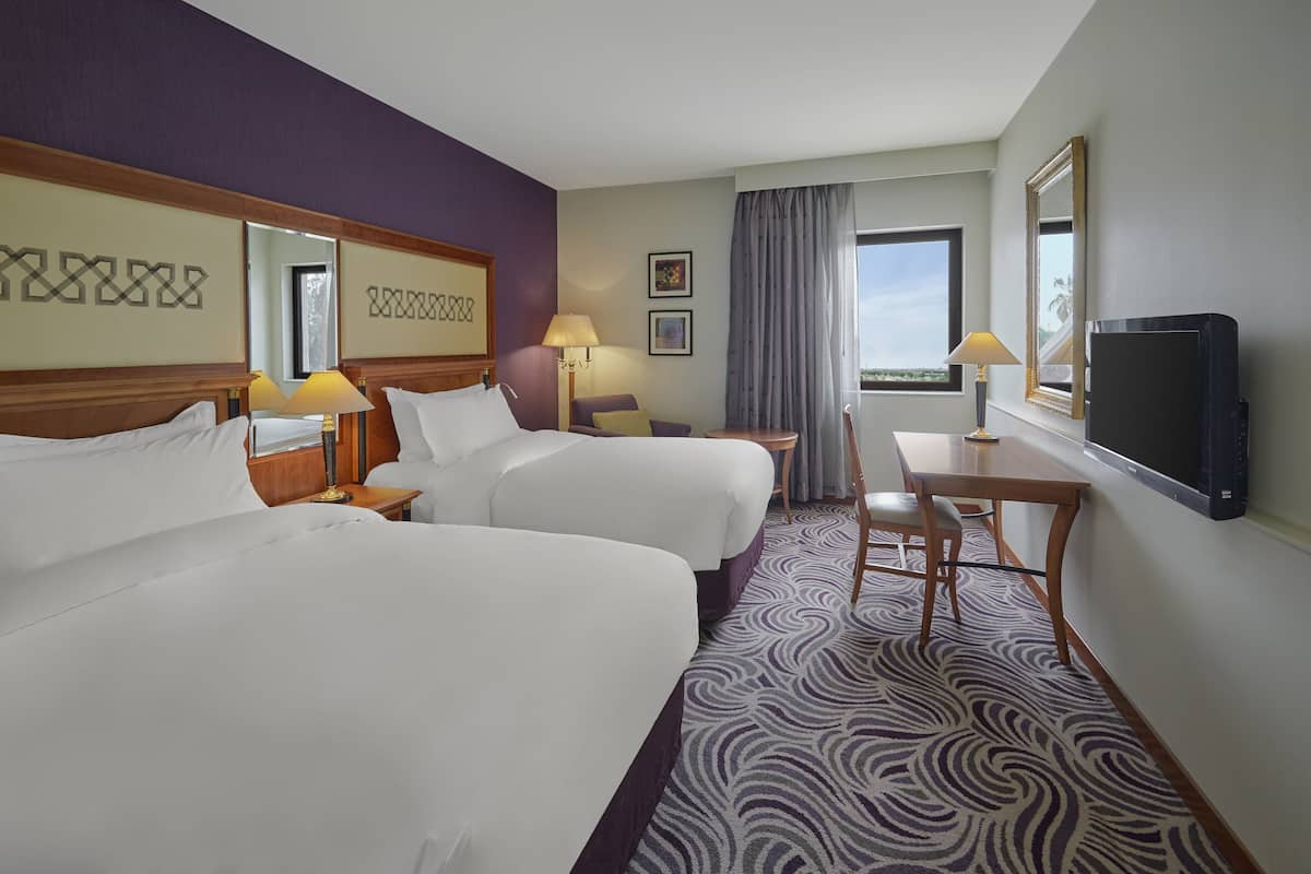 Ett hotellrum med två sängar, ett skrivbord, en stol, en TV och ett fönster med utsikt.