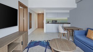 A modern living room with a flat-screen TV, wooden furniture, a blue sofa, and a kitchen area in the background. - Holiday Inn Tabuk by IHG (Tabuk)