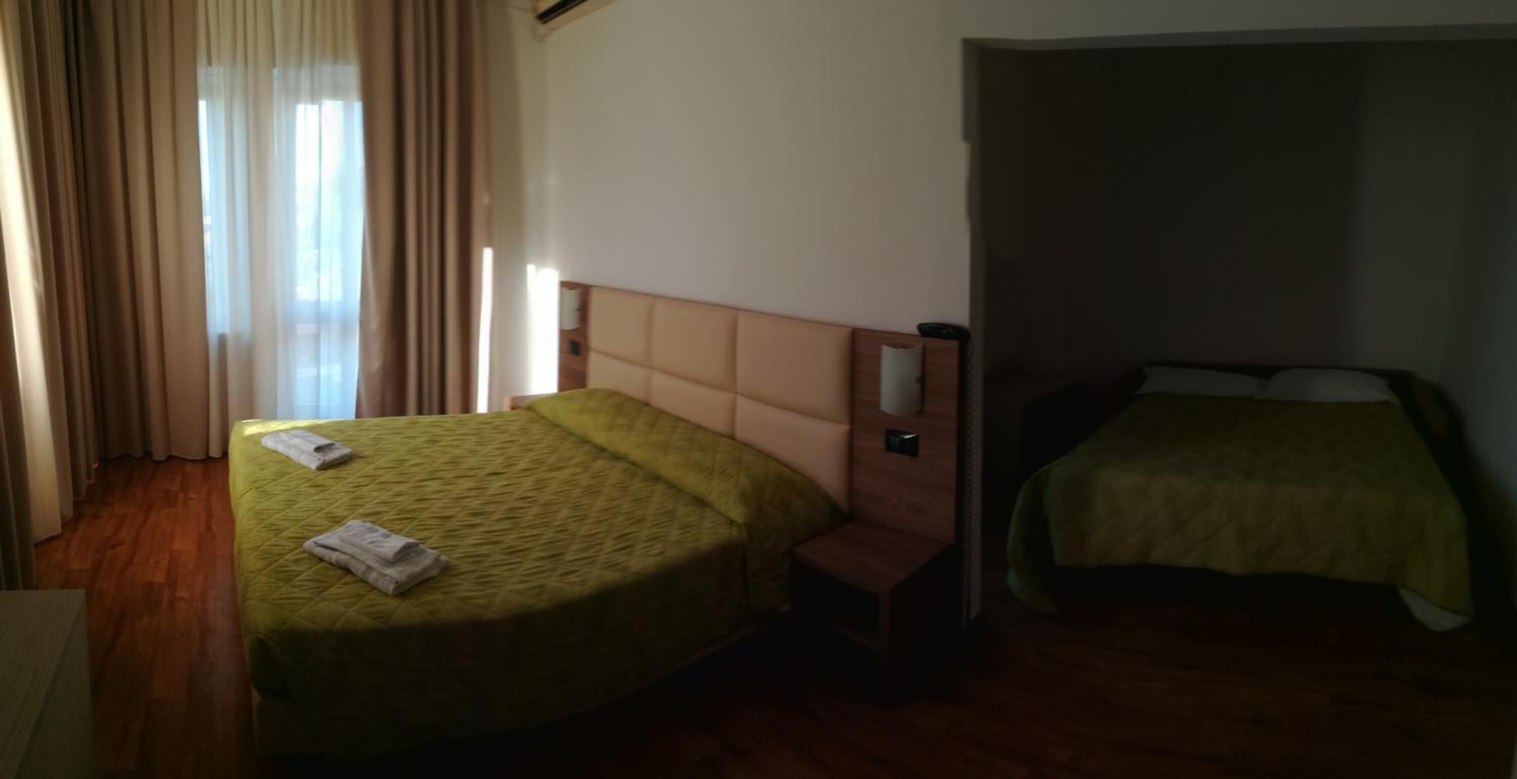 A hotel room with two beds, wooden flooring, and a window with curtains.