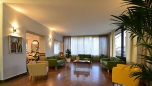 Un salon spacieux avec un canapé vert, un fauteuil jaune et une table basse. Il y a une grande fenêtre avec des rideaux, un tableau au mur et une plante en pot.