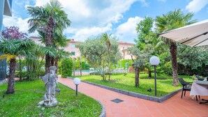 Une cour agrémentée d’une statue, de palmiers, d’une piscine et de coins salons extérieurs.
