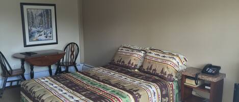 A bedroom with a bed, a desk, two chairs, a ceiling fan, and a telephone on a small table.