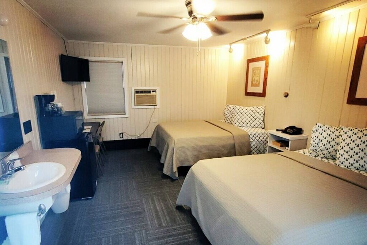 A hotel room with two beds, a ceiling fan, a TV, a sink, and a mirror.