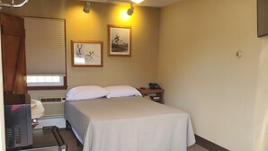 A hotel room with a bed, a desk with a computer, a ceiling fan, and two wall-mounted lights.
