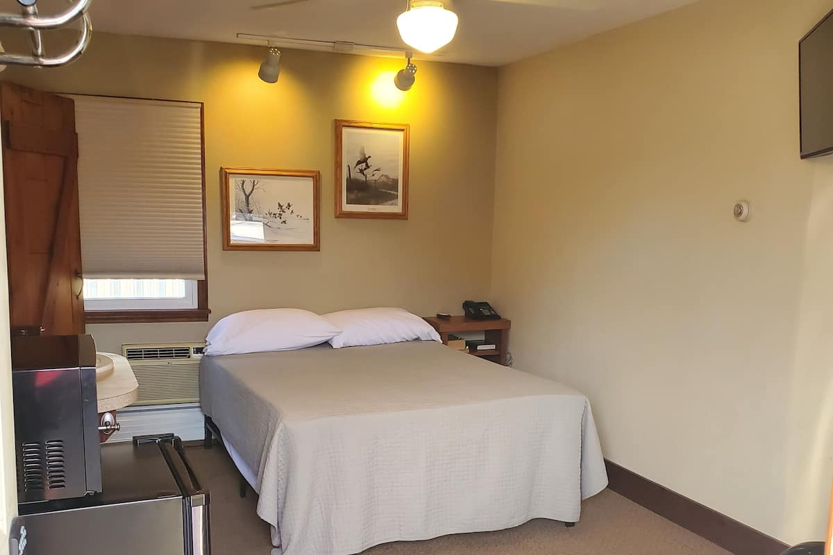 A hotel room with a bed, a desk with a computer, a ceiling fan, and two wall-mounted lights.