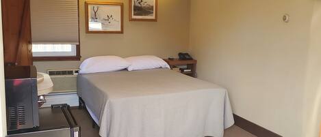 Habitación de hotel con cama, escritorio con computadora, ventilador de techo y dos luces fijadas a la pared.